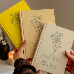 Peut inclure: Trois journaux à couverture rigide en jaune, beige et crème. Chaque journal présente une illustration florale et du texte. Le journal jaune porte le mot "LE". Le journal beige porte le mot "LETTRE". Le journal crème porte le texte "LETTRES À MA FILLE Chère Élisa".
