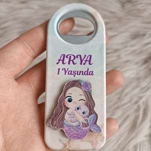Puede incluir: Un abridor de botellas blanco y azul con un dise&ntilde;o de sirena y el texto "ARYA 1 Yasunda".