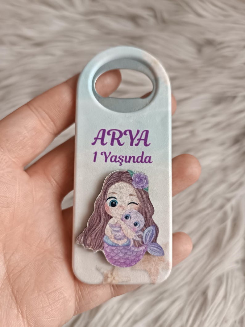 Puede incluir: Un abridor de botellas blanco y azul con un dise&ntilde;o de sirena y el texto "ARYA 1 Yasunda".