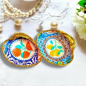 Op de afbeelding: Twee decoratieve schelpen met goud geschilderde randen. De binnenkant heeft handgeschilderde fruitontwerpen: een met sinaasappels en de andere met citroenen. De schalen staan op een witte achtergrond met parels en kant.