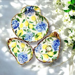 Op de afbeelding: Een set van drie keramische mokken met een gespikkelde, matte afwerking. De mokken zijn in crème, lichtgrijs en donkergrijs. Elke mok heeft een eenvoudig, minimalistisch ontwerp.