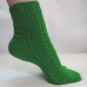 May include: A green knitted sock with a cable knit pattern. The sock is shown on a foot, with the heel and toe visible.