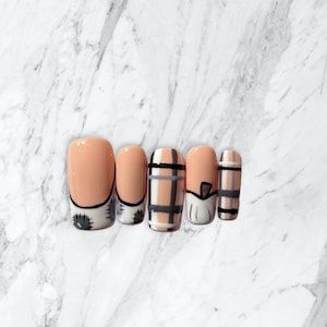 May include: Five artificial nails with a peach-colored base. Two nails have a black and white design at the base. One nail has a plaid pattern in black, gray, and peach. The other two nails have a black and gray striped design.