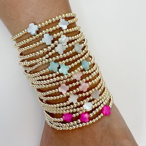May include: A stack of gold bead bracelets with cross charms. The charms are in various colors, including white, pink, and light blue.