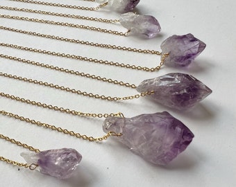 May include: Multiple gold chains with amethyst crystal pendants. The crystals are various sizes and shapes, with some being clear and others having a purple hue.