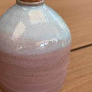 Peut inclure: Une burette à huile en céramique avec un corps arrondi et un émail bicolore. La partie supérieure est d'un bleu clair doux, passant à un rose vieux rose sur la moitié inférieure. Le récipient est surmonté d'un bouchon en liège et d'un bec verseur.