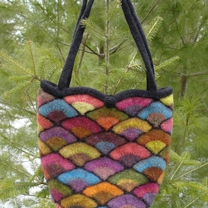 Könnte beinhalten: Eine bunte gestrickte Tragetasche mit einem schwarzen Henkel und einer gewellten Oberseite. Die Tasche ist aus verschiedenenfarbigen Garnen gefertigt, darunter Rot, Orange, Gelb, Grün, Blau, Lila und Braun.