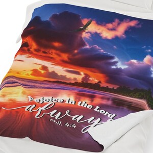 May include: A throw blanket with a colorful sunset over a tropical beach. The text "Rejoice in the Lord always Phil. 4:4" is printed on the blanket.