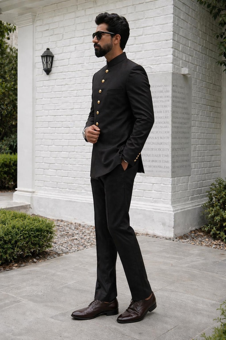 Puede incluir: Un traje negro con una chaqueta de cuello mandar&iacute;n y pantalones a juego. La chaqueta tiene botones dorados y mangas largas. El conjunto se combina con zapatos de vestir de cuero marr&oacute;n. El traje es un conjunto formal.