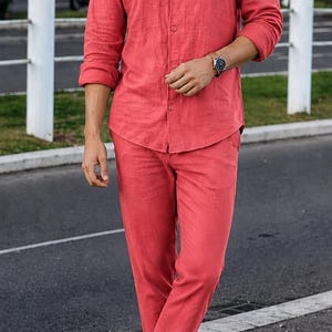 May include: A coral-coloured long-sleeved button-down shirt with a mandarin collar and matching straight-leg trousers. The outfit is paired with dark navy blue slip-on shoes. The fabric appears to have a textured, linen-like weave throughout.