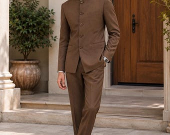 Puede incluir: Un traje marrón con cuello mao, pantalones a juego y mocasines marrones. El traje presenta un corte entallado y se lleva con una camisa blanca con cuello. El conjunto es adecuado para ocasiones formales.