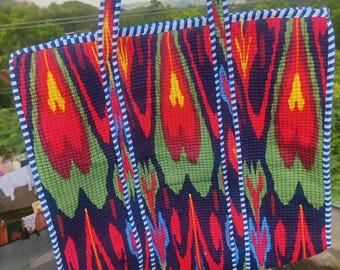 May include: A patterned tote bag featuring a design in red, green, yellow, and blue. The bag has strong handles and a blue and white striped trim. The bag is made of woven fabric and is suitable for carrying shopping or other items.