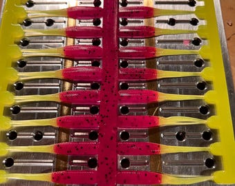 May include: A mold with multiple rows of yellow and pink plastic fishing lures. The lures are in a mold with metal rods and holes.