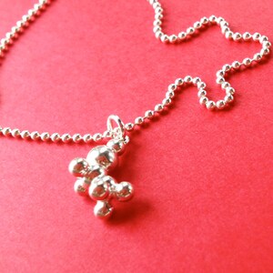 May include: A silver necklace with a round chain and a pendant shaped like a cluster of spheres.