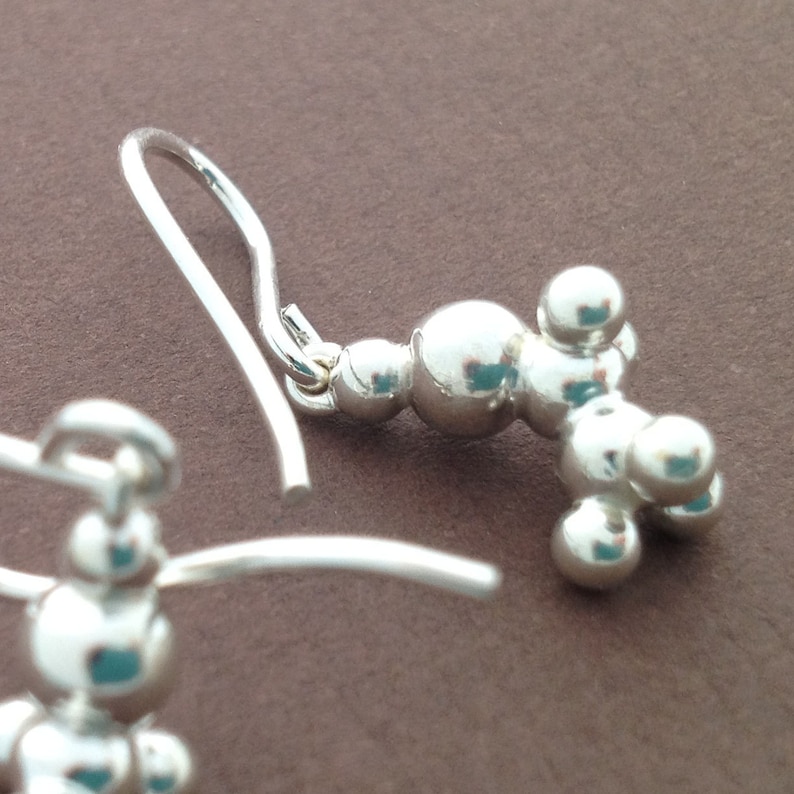 May include: Silver dangle earrings with a cluster of small round beads in a geometric shape.