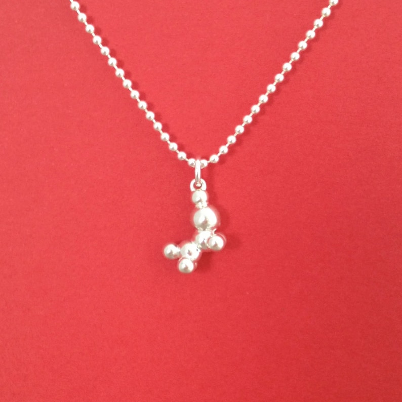 May include: A silver chain necklace with a silver pendant shaped like a stylized dog. The pendant is made of multiple round beads.