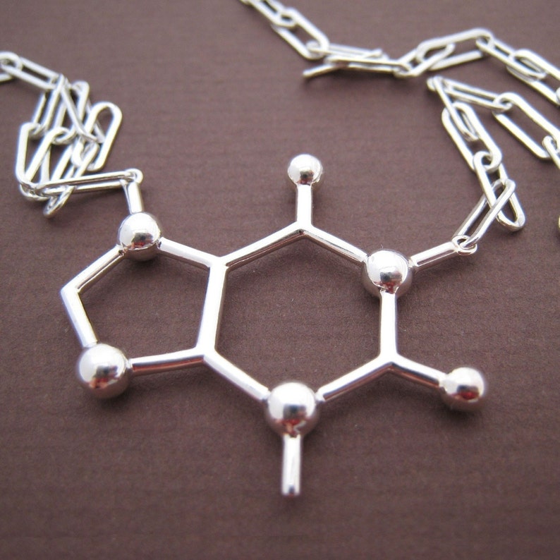 Puede incluir: Collar de plata con un colgante en forma de mol&eacute;cula de cafe&iacute;na. El colgante est&aacute; hecho de alambre de plata y tiene un acabado brillante.