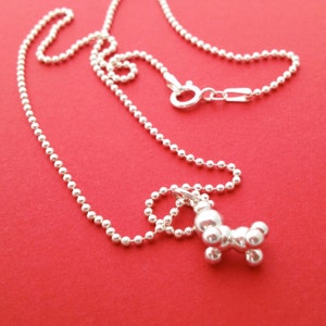 May include: A silver necklace with a silver pendant shaped like a cluster of round balls. The necklace is on a red background.