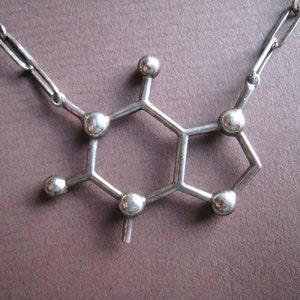 Puede incluir: Un collar de plata con un colgante en forma de mol&eacute;cula de cafe&iacute;na.