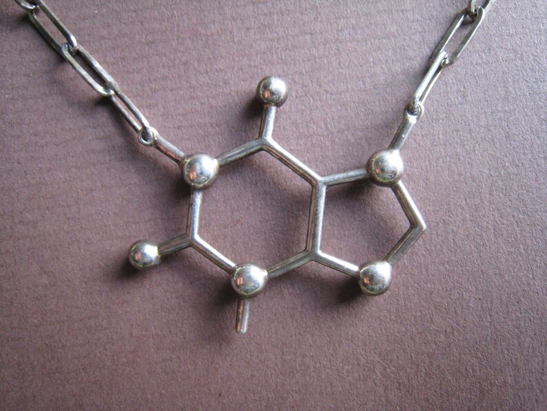 Puede incluir: Un collar de plata con un colgante en forma de mol&eacute;cula de cafe&iacute;na.