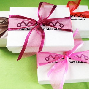 May include: Three white gift boxes with pink, red, and brown ribbon bows. The boxes are stacked on top of each other. The top box has the text "made with molecules" printed on it.