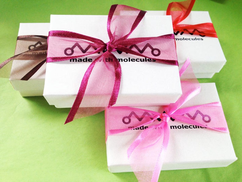 May include: Three white gift boxes with pink, red, and brown ribbon bows. The boxes are stacked on top of each other. The top box has the text "made with molecules" printed on it.