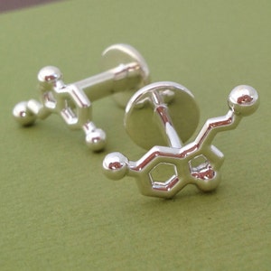 May include: A pair of silver cufflinks shaped like a chemical molecule. The cufflinks are detailed and have a shiny finish.