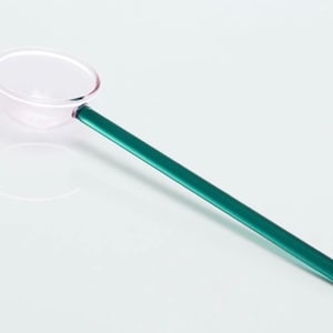 Könnte beinhalten: Ein durchsichtiger Glaslöffel mit einem türkisfarbenen Griff. Der Löffel hat eine abgerundete Schale und einen langen, schlanken Griff.