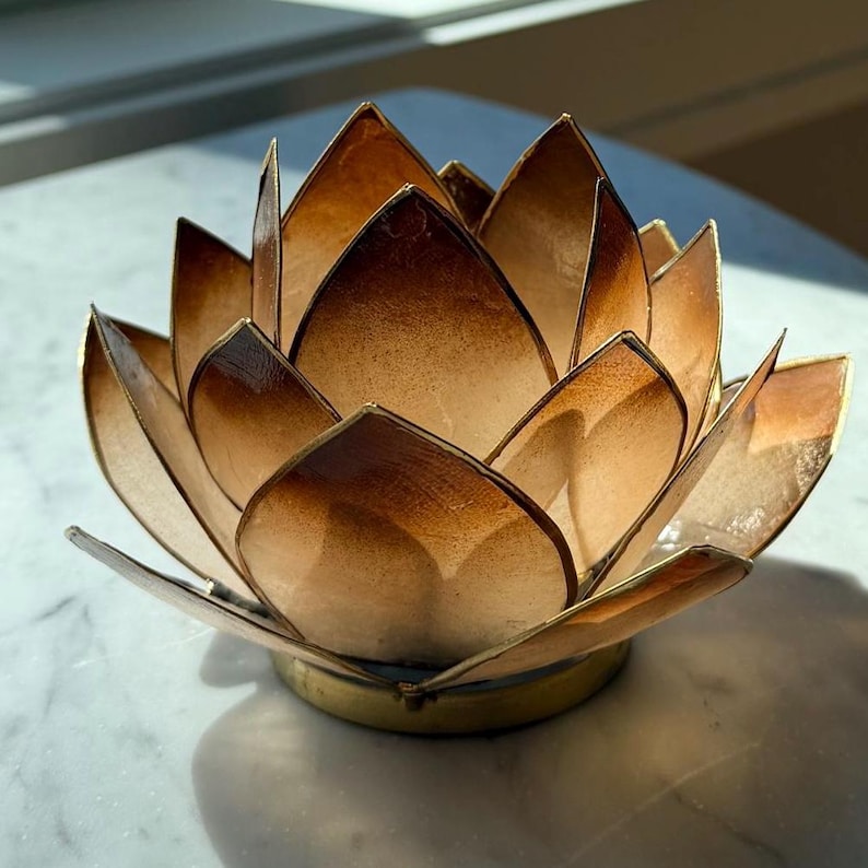 May include: A decorative lotus flower candle holder. The petals are a gradient of brown and gold, with a metallic gold trim. The base is a gold-colored metal. The candle holder is designed to hold a small candle.