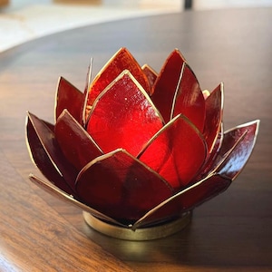 May include: A red lotus flower candle holder with gold trim. The petals are a deep red with a metallic sheen, and the edges are outlined in gold. The base is a matching gold color, creating a striking contrast.