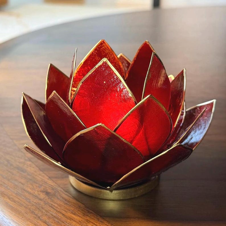 May include: A red lotus flower candle holder with gold trim. The petals are a deep red with a metallic sheen, and the edges are outlined in gold. The base is a matching gold color, creating a striking contrast.