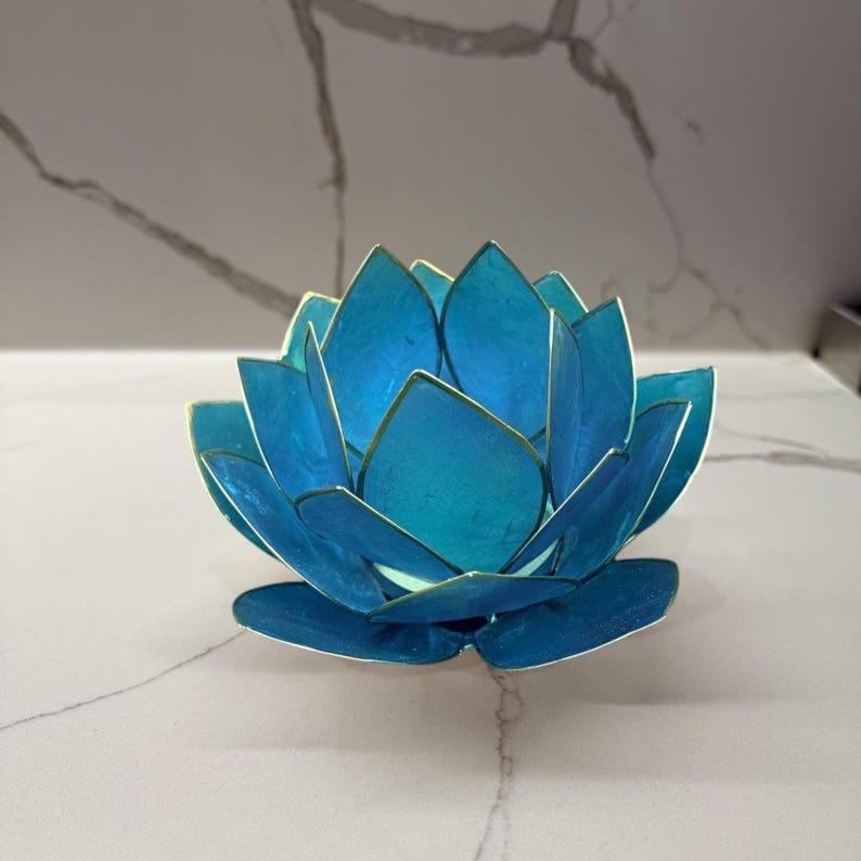 May include: A handcrafted, blue lotus flower-shaped candle holder with gold trim. The petals are a gradient of blue hues, creating a visually appealing and serene decorative piece. The candle holder is designed to hold a small candle.