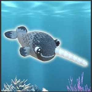 May include: A gray and white crocheted narwhal plush toy with a white spiral horn. The toy is swimming in a blue water background with coral reefs.