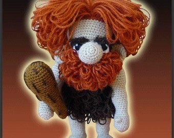 May include: A crocheted plush toy of a caveman with a club. The caveman has a red beard and hair, a white face, and a brown loincloth.