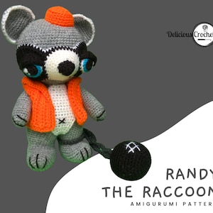 Puede incluir: Patrón de amigurumi de crochet para Randy el mapache, un mapache gris que lleva un chaleco naranja y un gorro rojo, sosteniendo una bola negra con costuras blancas. El patrón se titula "Randy the Raccoon Amigurumi Pattern".