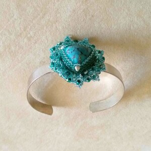 May include: A silver bangle bracelet with a turquoise gemstone set in a green beaded design.