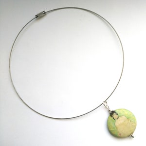 May include: A silver chain necklace with a round pendant featuring a painting of a person. The pendant is green, white, and beige.