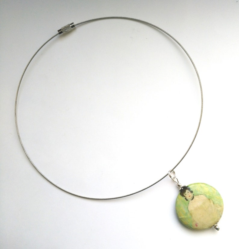 May include: A silver chain necklace with a round pendant featuring a painting of a person. The pendant is green, white, and beige.