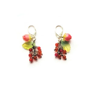 May include: A pair of silver earrings with pink and green flower charms and red and orange beads.