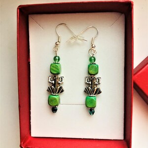 May include: A pair of green and silver frog earrings in a red box. The earrings feature green wooden beads and a silver frog charm.