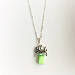 May include: A silver chain necklace with a green and silver angel pendant. The angel has wings and a pearl bead in the center.