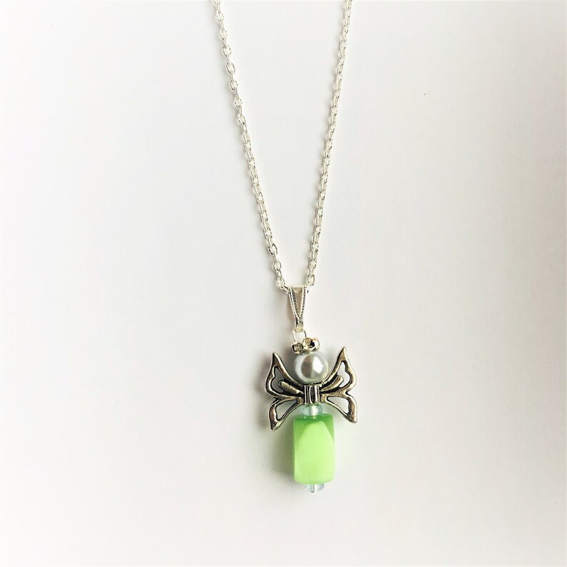 May include: A silver chain necklace with a green and silver angel pendant. The angel has wings and a pearl bead in the center.