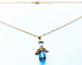 May include: A gold chain necklace with a blue crystal angel pendant. The angel has a white pearl and blue crystal accents.
