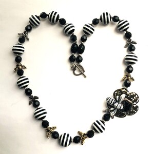May include: Black and white striped beads with black crystal beads and gold bee charms make up this necklace. The necklace has a silver clasp.