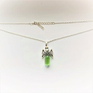 May include: A silver chain necklace with a green glass angel pendant. The angel has silver wings and a white pearl bead for a head.
