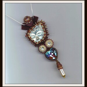 May include: A silver pendant with a face design, surrounded by red and gold beads, with a heart-shaped crystal and a pearl hanging below.