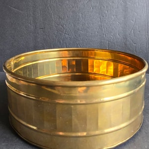 May include: A round, gold-colored brass planter with a ribbed design. The planter is empty and has a shiny finish.