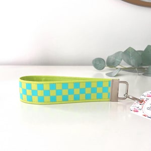 May include: A lime green and light blue checkered key chain with a silver key ring.