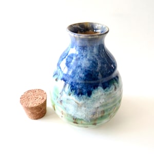 May include: A handmade ceramic vase with a cork stopper. The vase features a gradient of colors, transitioning from deep blue at the top to light blue and green at the base. The cork stopper is a light brown color.