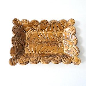 May include: A rectangular ceramic dish with a scalloped edge and a floral design. The dish is glazed in a brown color.